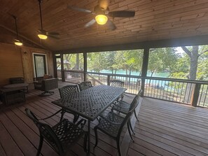 Een overdekt terras buiten met een tafel, stoelen, een plafondventilator en uitzicht op water.