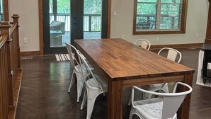 A dining area with a wooden table and white chairs, large windows with blinds, and a hanging light fixture. - Charming Modern Craftsman Right on the Water (Linn Valley)