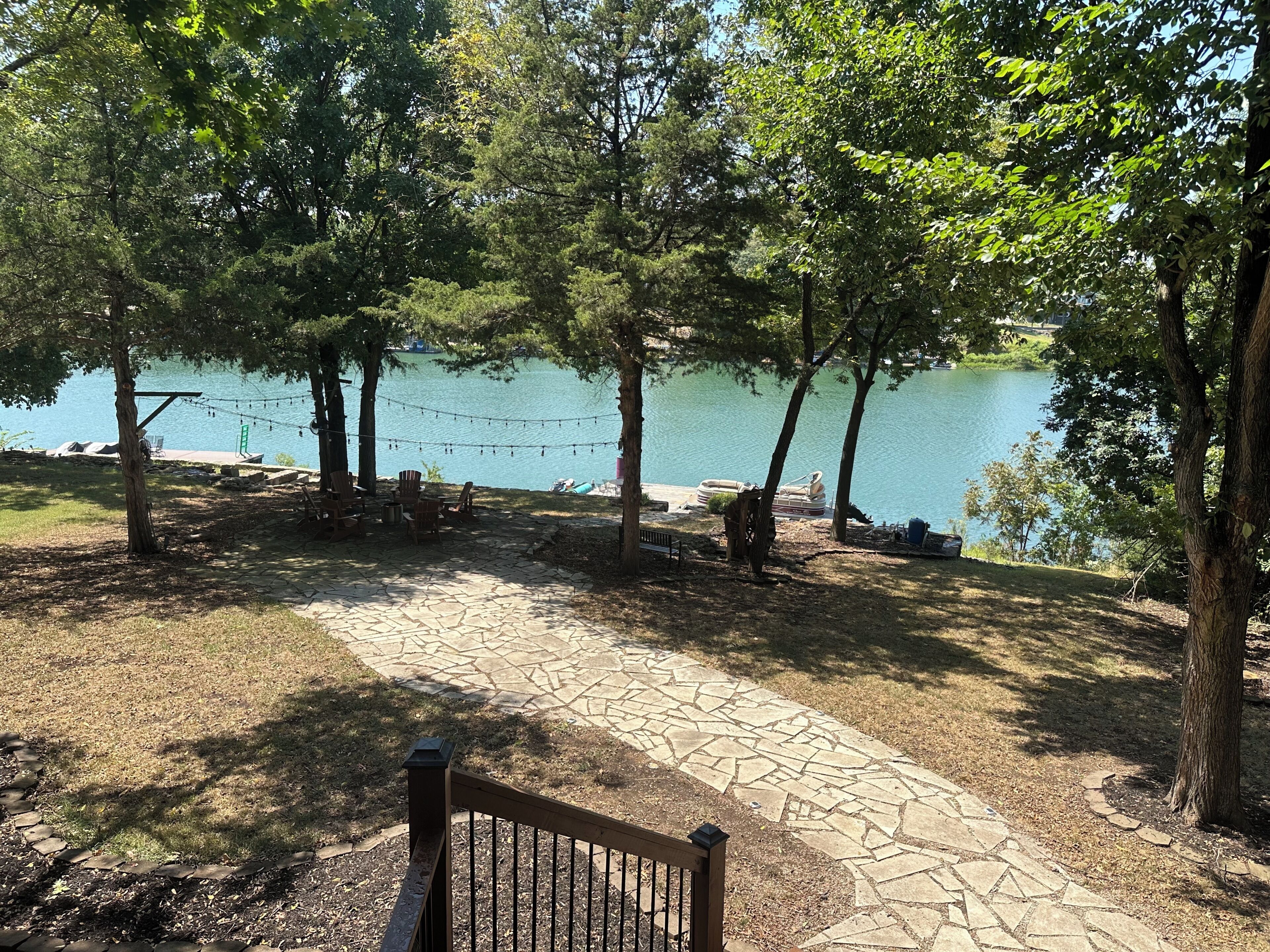 Un patio junto al lago con suelo de piedra, sillas de madera y un banco.