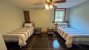A bedroom with two beds, a ceiling fan, a window with blinds, and a small table. - Charming Modern Craftsman Right on the Water (Linn Valley)