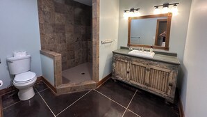 A bathroom with a shower, toilet, vanity, and a mirror with lights. - Charming Modern Craftsman Right on the Water (Linn Valley)