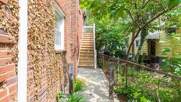 A brick building with a wooden staircase leading to a door, surrounded by greenery and a chain-link fence.