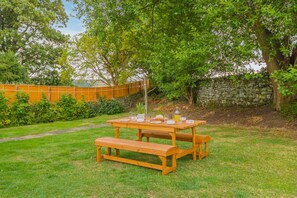 Una mesa de picnic de madera al aire libre con bancos, rodeada de césped y árboles.