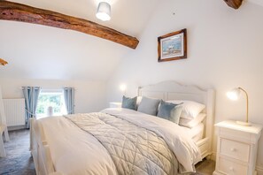 Ein Schlafzimmer mit einem großen Bett, einem Nachttisch, einer Nachttischlampe, einem gerahmten Bild an der Wand und einem Fenster mit Vorhängen.