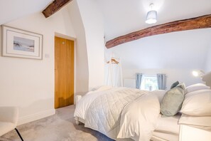 Un dormitorio con una cama, una puerta de madera, una pared blanca y una viga en el techo.