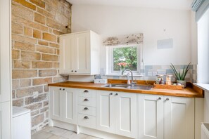 A kitchen with white cabinets, a wooden countertop, a window with a view of greenery, and a sign on the wall. - 4 Bed in Ainthorpe (oc-m45794) (Danby)