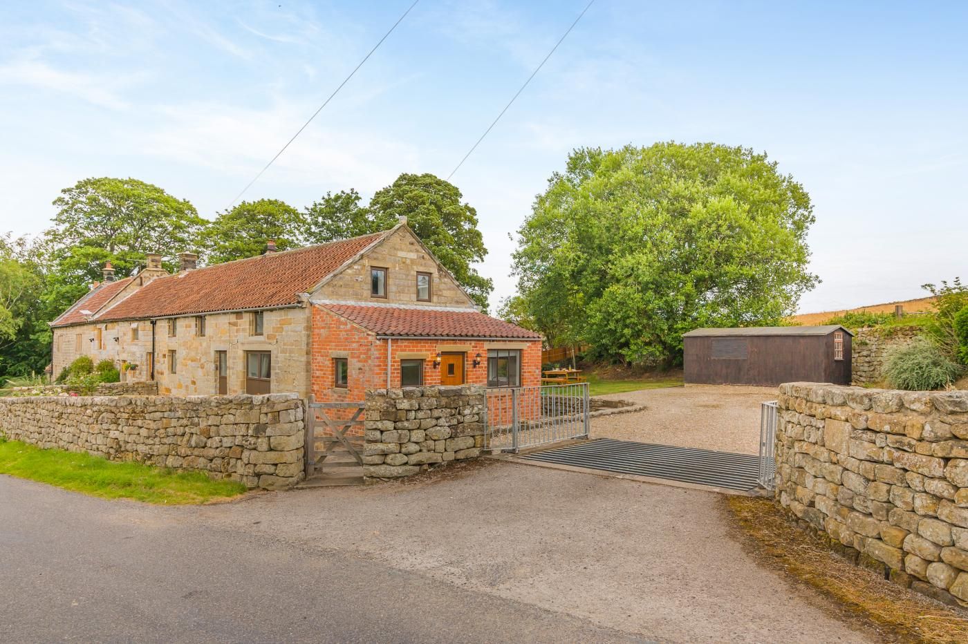 A stone house with a red-tiled roof, a wooden gate, and a gravel driveway.