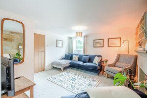 Ein Wohnzimmer mit Sofa, Sessel, Fernseher, Teppich und Kamin.