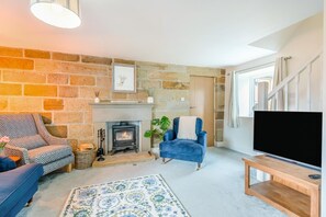 Una sala de estar con chimenea de piedra, un televisor, un sillón azul y un tapete estampado.