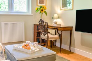 A cozy living room with a white radiator, a wooden table with a lamp, a bookshelf, and a flat-screen TV mounted on the wall. - 1 Bed in Frampton Mansell (oc-t45435) (Frampton Mansell)