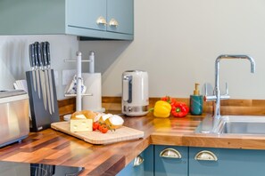 A modern kitchen with a wooden countertop, a cutting board with cheese and tomatoes, a toaster, and a sink. - 1 Bed in Frampton Mansell (oc-t45435) (Frampton Mansell)
