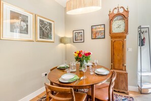 A dining area with a round table set for four, framed pictures on the wall, a tall floor lamp, and a grandfather clock. - 1 Bed in Frampton Mansell (oc-t45435) (Frampton Mansell)