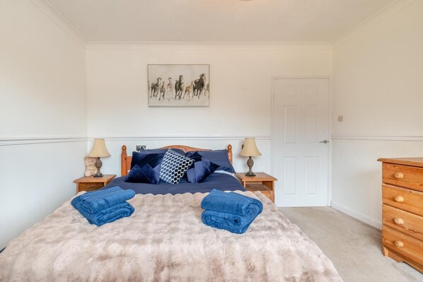 Une chambre à coucher comprenant un lit, deux tables de chevet, une commode en bois et un tableau accroché au mur.