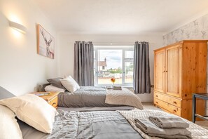 A bedroom with two beds, a wooden wardrobe, a bedside table with a lamp, and a window with curtains.