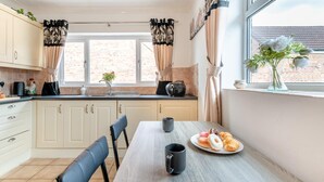A kitchen with a dining table, chairs, a coffee maker, and a plate of pastries. - 2 Bed in Middle Rasen (oc-c45686) (Middle Rasen)