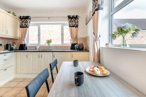 A kitchen with a dining table, chairs, a coffee maker, and a plate of pastries. - 2 Bed in Middle Rasen (oc-c45686) (Middle Rasen)
