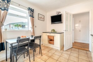 A compact kitchen with a dining area, a flat-screen TV mounted above the counter, and a view of the outside through the window.
