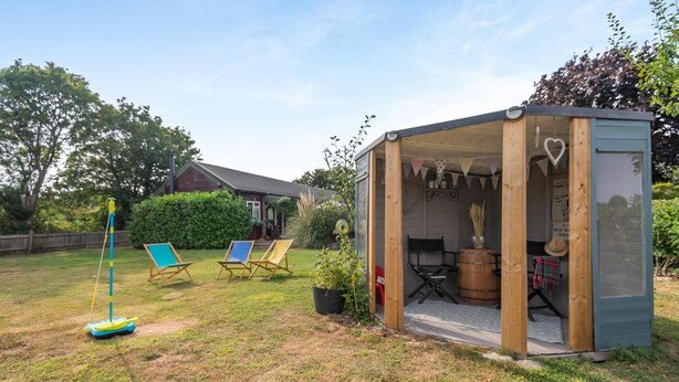 A small wooden structure with a glass door, a sailboat, and two lawn chairs in a backyard. - 3 Bed in Marden (oc-l45561) (Horsmonden)