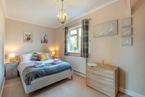 A bedroom with a bed, bedside tables, a dresser, a window with curtains, and wall art.