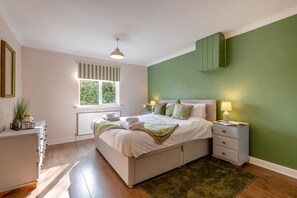 Ein Schlafzimmer mit einem Bett, Nachttischen, einem Fenster und einer grünen Wand.