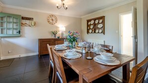 A dining room with a wooden table set for four, a chandelier, a clock, and a wall-mounted plate rack. - 3 Bed in Marden (oc-l45561) (Horsmonden)