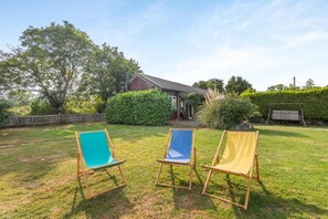A backyard with three wooden chairs, a wooden fence, and a house with a porch.