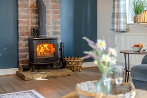A cozy living room with a brick fireplace, a wooden table with a bowl of fruit, and a blue wall.