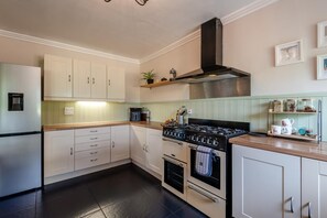 A modern kitchen with white cabinets, a stainless steel range hood, and a built-in oven.