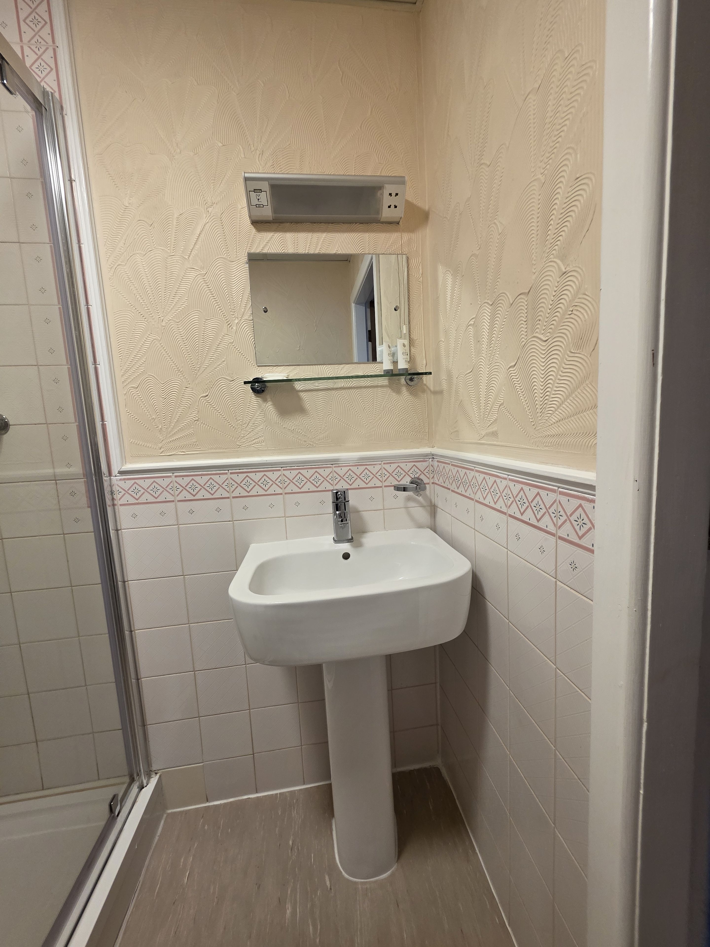 Un baño con lavamanos blanco, un espejo y cabina de ducha.