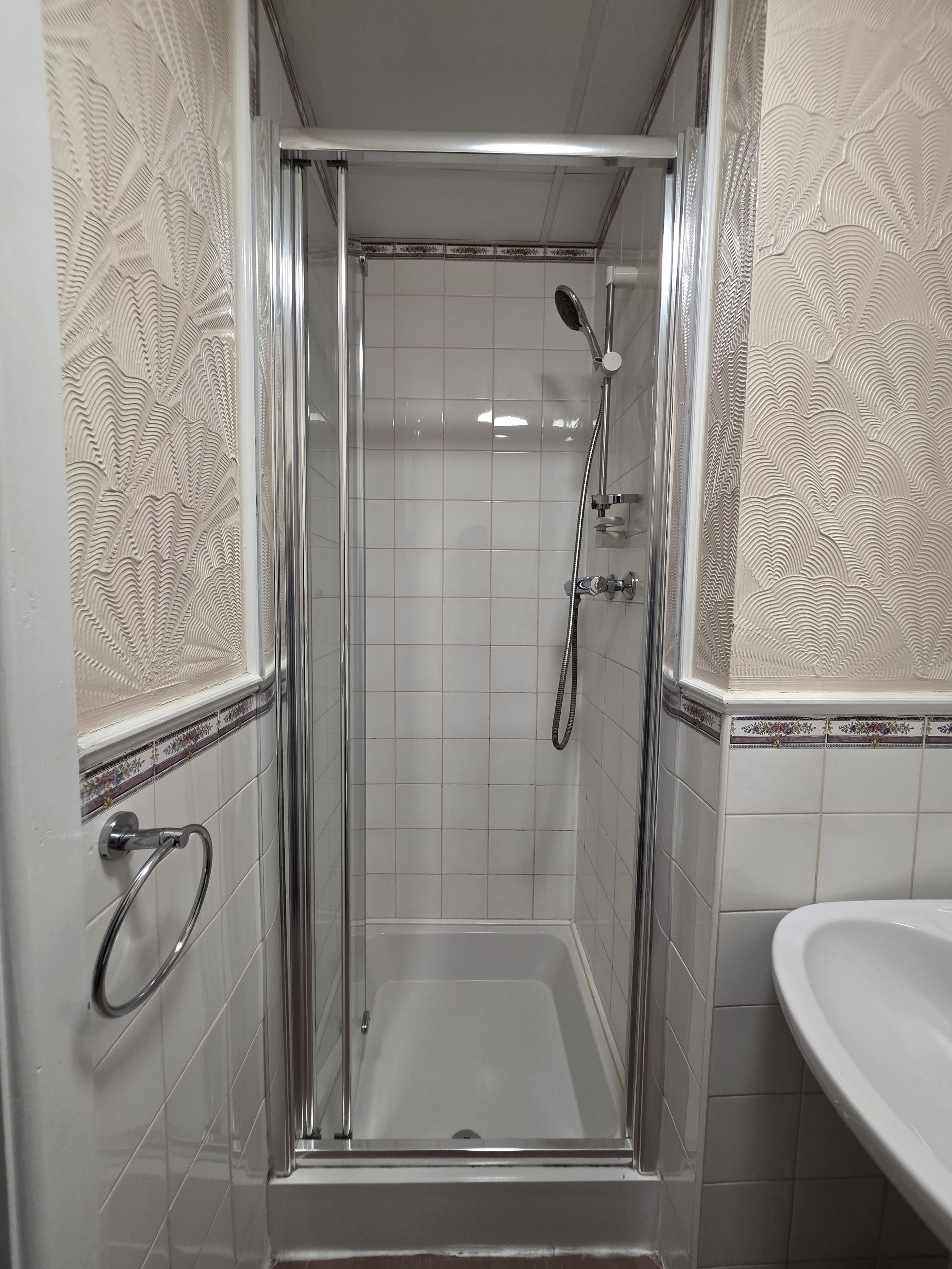 A shower enclosure with a glass door, a handheld showerhead, and a handheld shower attachment.