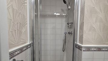 A shower enclosure with a glass door, a handheld showerhead, and a handheld shower attachment.