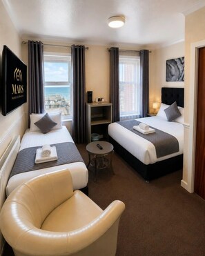 Habitación de hotel con dos camas, un sofá, una mesita y vista al mar.