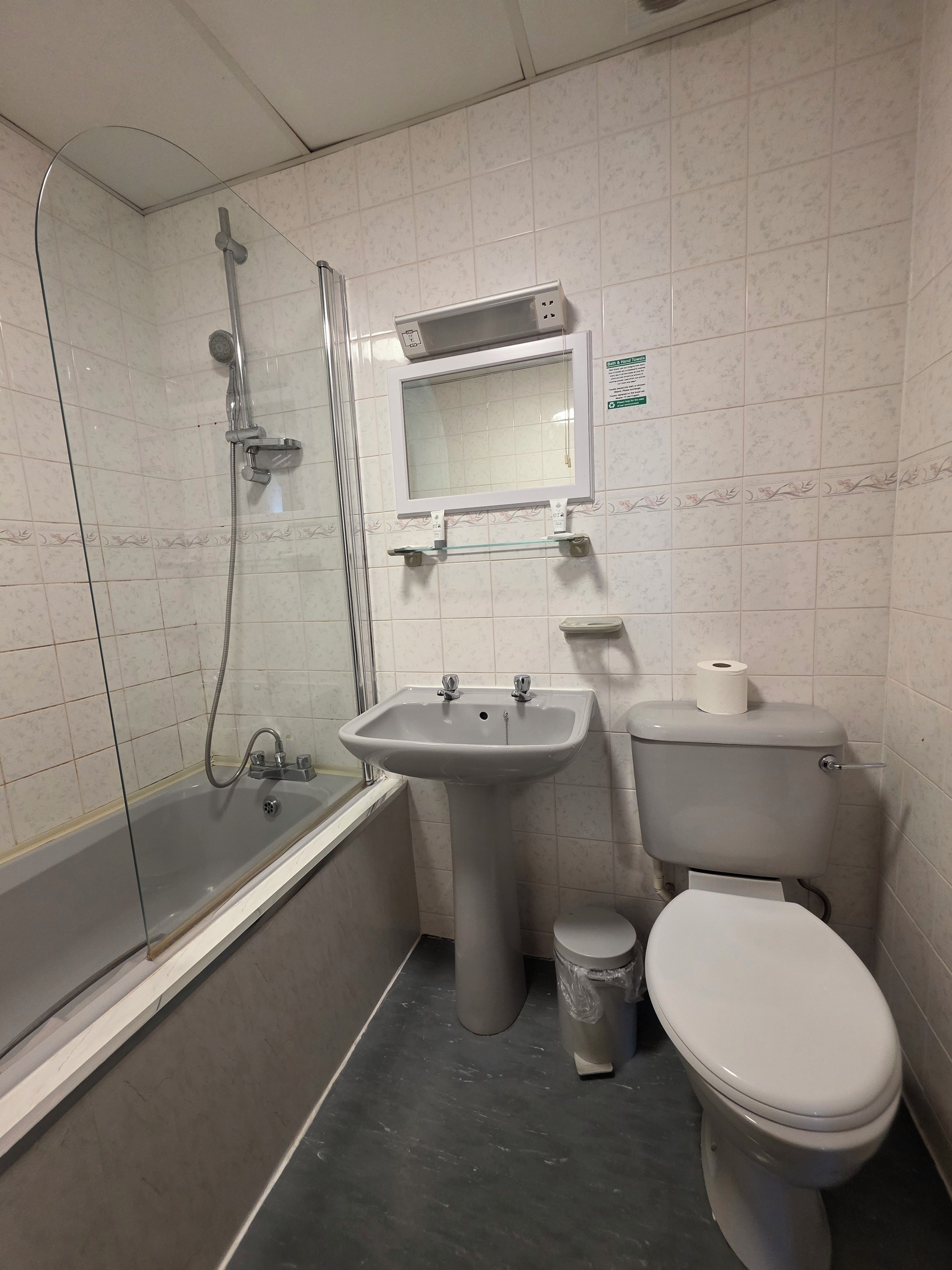 A bathroom with a glass-enclosed shower, a pedestal sink, a toilet, and a small trash bin.