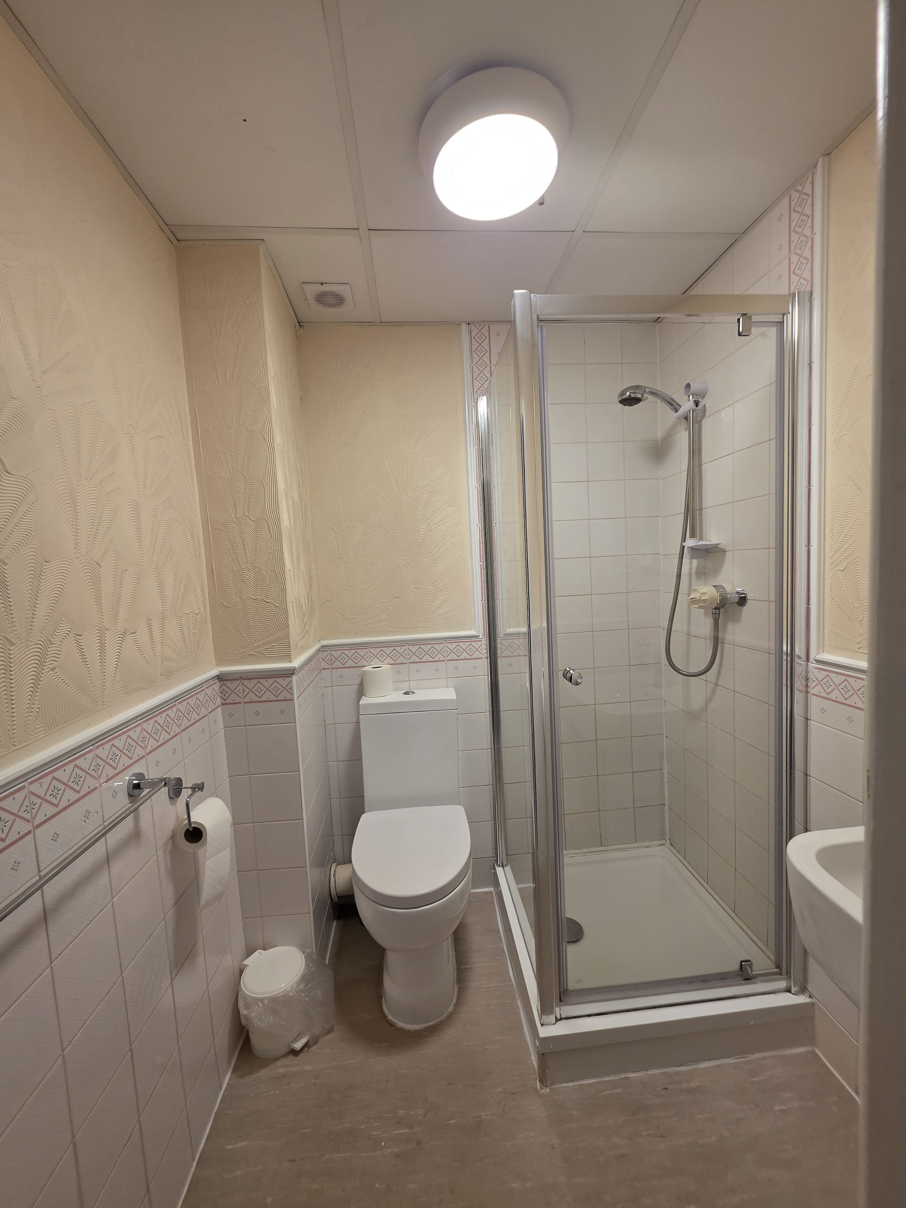 A bathroom with a toilet, a shower enclosure, and a toilet paper holder.