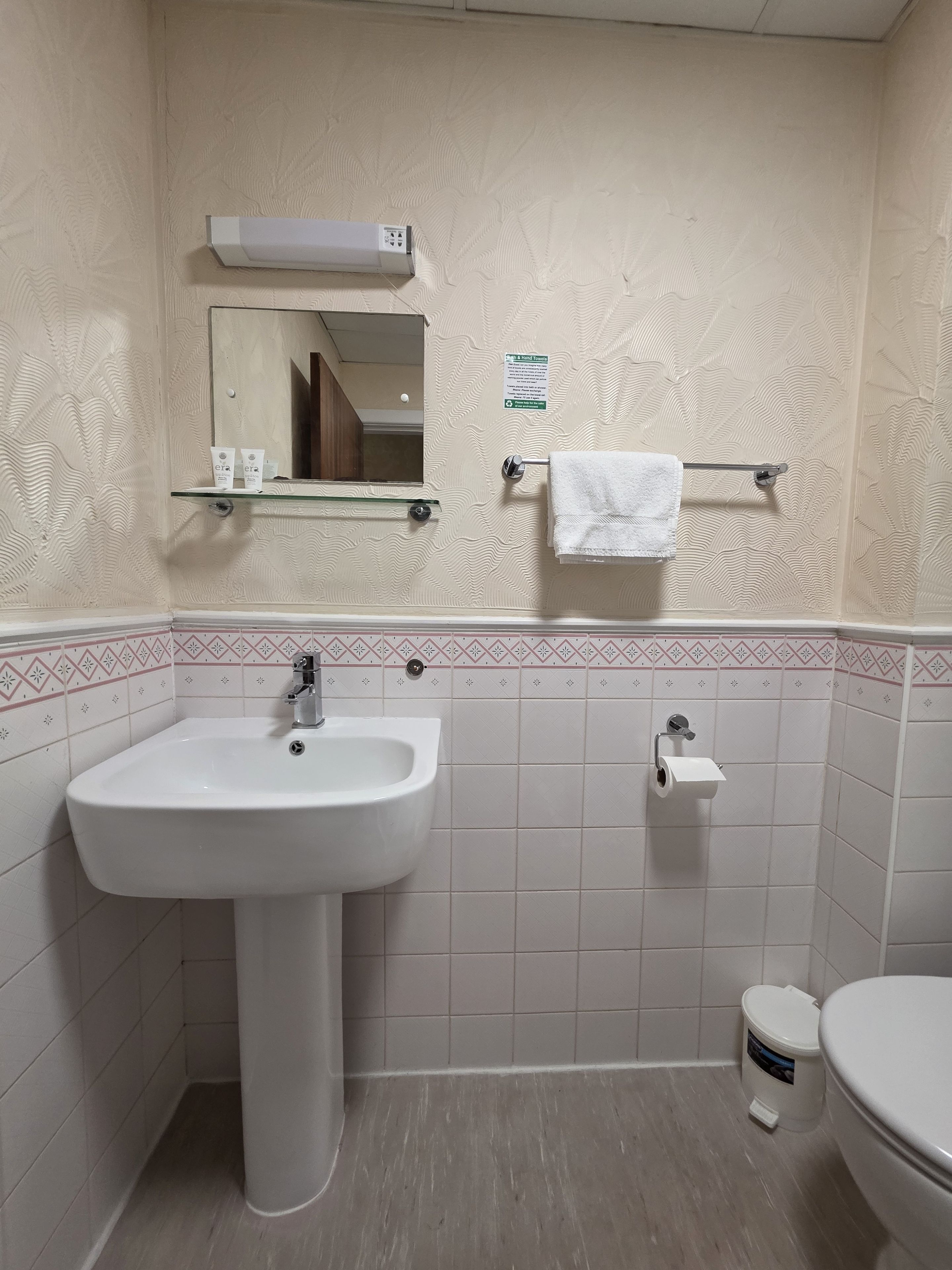 A bathroom with a white sink, mirror, and toilet. There is a towel rack with a white towel.