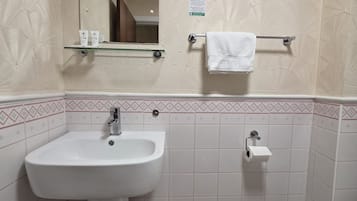 A bathroom with a white sink, mirror, and toilet. There is a towel rack with a white towel.