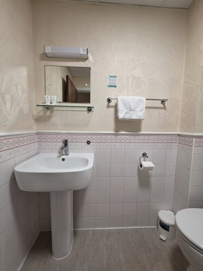 Un baño con lavamanos blanco, espejo y retrete. Hay un toallero con una toalla blanca.