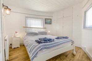 Quarto com cama, luminárias de cabeceira, janela com persianas, radiador e guarda-roupa.