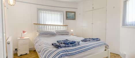 Une chambre à coucher comprenant un lit, des lampes de chevet, une fenêtre avec des stores, un radiateur et une armoire.