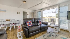 A cozy living room with a leather sofa, white chairs, a dining table, and a balcony with a view. - 3 Bed in Heacham (oc-v45689) (The Beach)