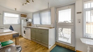 A compact kitchen with a washing machine, a sink, and a wooden table. - 3 Bed in Heacham (oc-v45689) (The Beach)