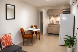 Ein kompakter Wohnbereich mit Essplatz, Küche und einer Couch mit dekorativem Kissen.