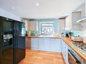A modern kitchen with a black refrigerator, white cabinets, a wooden countertop, a gas stove, and a window with blinds. - 4 Bed in Westward Ho (oc-o45219) (Northam)