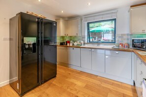 A modern kitchen with a double-door refrigerator, a built-in water dispenser, and a window with a view of the outdoors. - 4 Bed in Westward Ho (oc-o45219) (Northam)