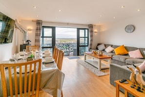 A modern living room with a dining area, a sofa set, and a view of the outdoors. - 4 Bed in Westward Ho (oc-o45219) (Northam)