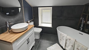Ein modernes Badezimmer mit einem großen Spiegel, einer freistehenden Badewanne und einer Toilette.