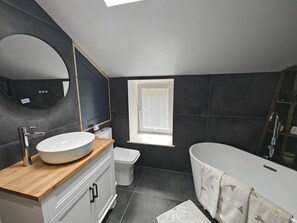 Ein modernes Badezimmer mit einem großen Spiegel, einer freistehenden Badewanne und einer Toilette.