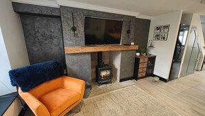 Ein modernes Wohnzimmer mit Kamin, einem an der Wand montierten Fernseher und einem bequemen orangefarbenen Sessel.