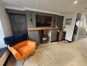 Ein modernes Wohnzimmer mit Kamin, einem an der Wand montierten Fernseher und einem bequemen orangefarbenen Sessel.