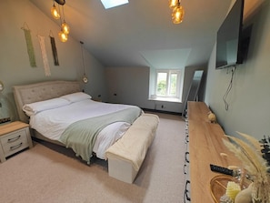 A bedroom with a large bed, a wooden dresser, a bench, a nightstand, a TV, and a window. - 1 Bed in Grizebeck (oc-s45852) (Kirkby Ireleth)